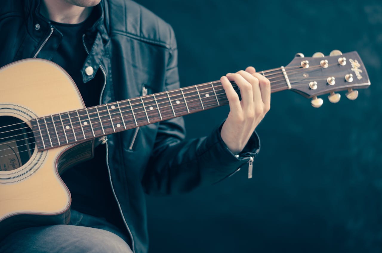 Close-up of a musician playing an acoustic guitar, wearing a leather jacket.