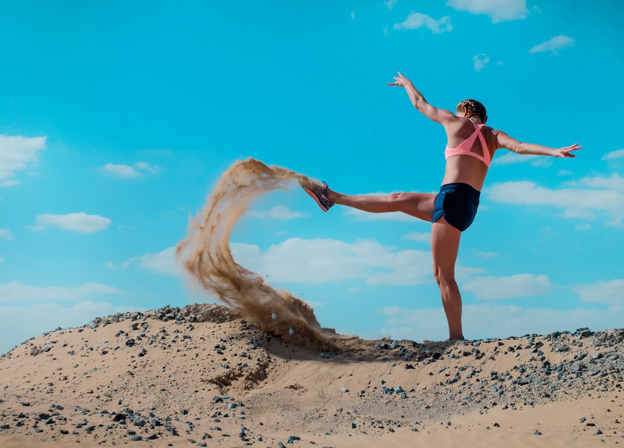 A lively scene of a woman kicking sand in the Dubai desert under a clear blue sky.