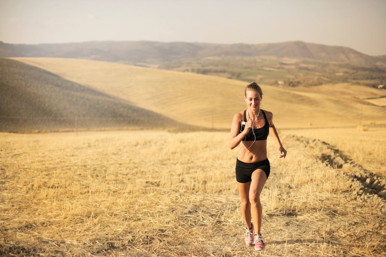Fit woman jogging in a sunny rural landscape with hills and dry grass.